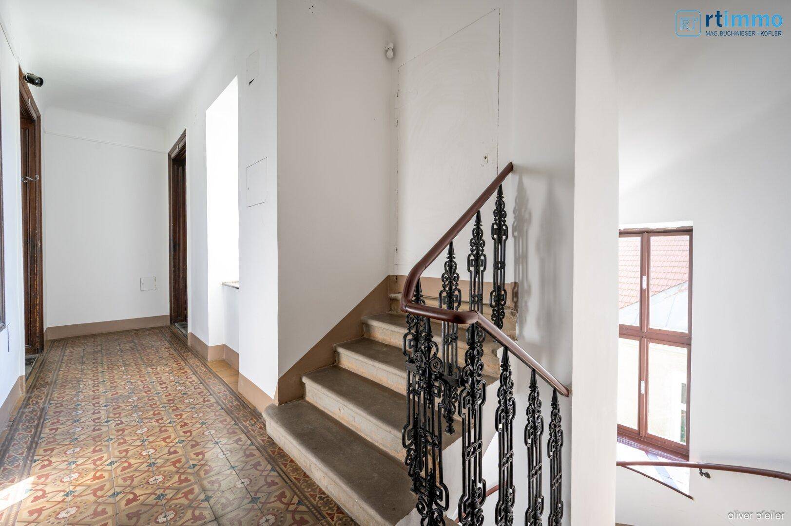 Historisches Treppenhaus mit kunstvollem Geländer und gemusterten Fliesen im Eingangsbereich.