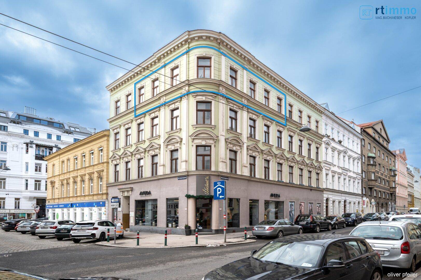 Historisches Eckgebäude in städtischer Umgebung mit klassischer Architektur und vielen Fenstern.
