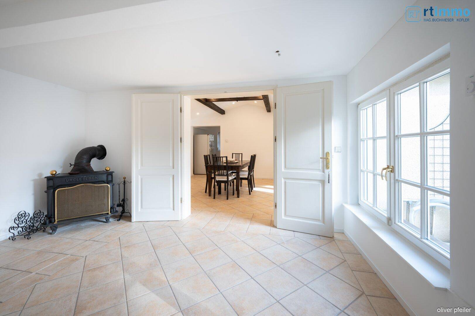 Wohnbereich mit Fliesenboden, dunklen Holzbalken an der Decke und offenem Durchgang zum Esszimmer.
