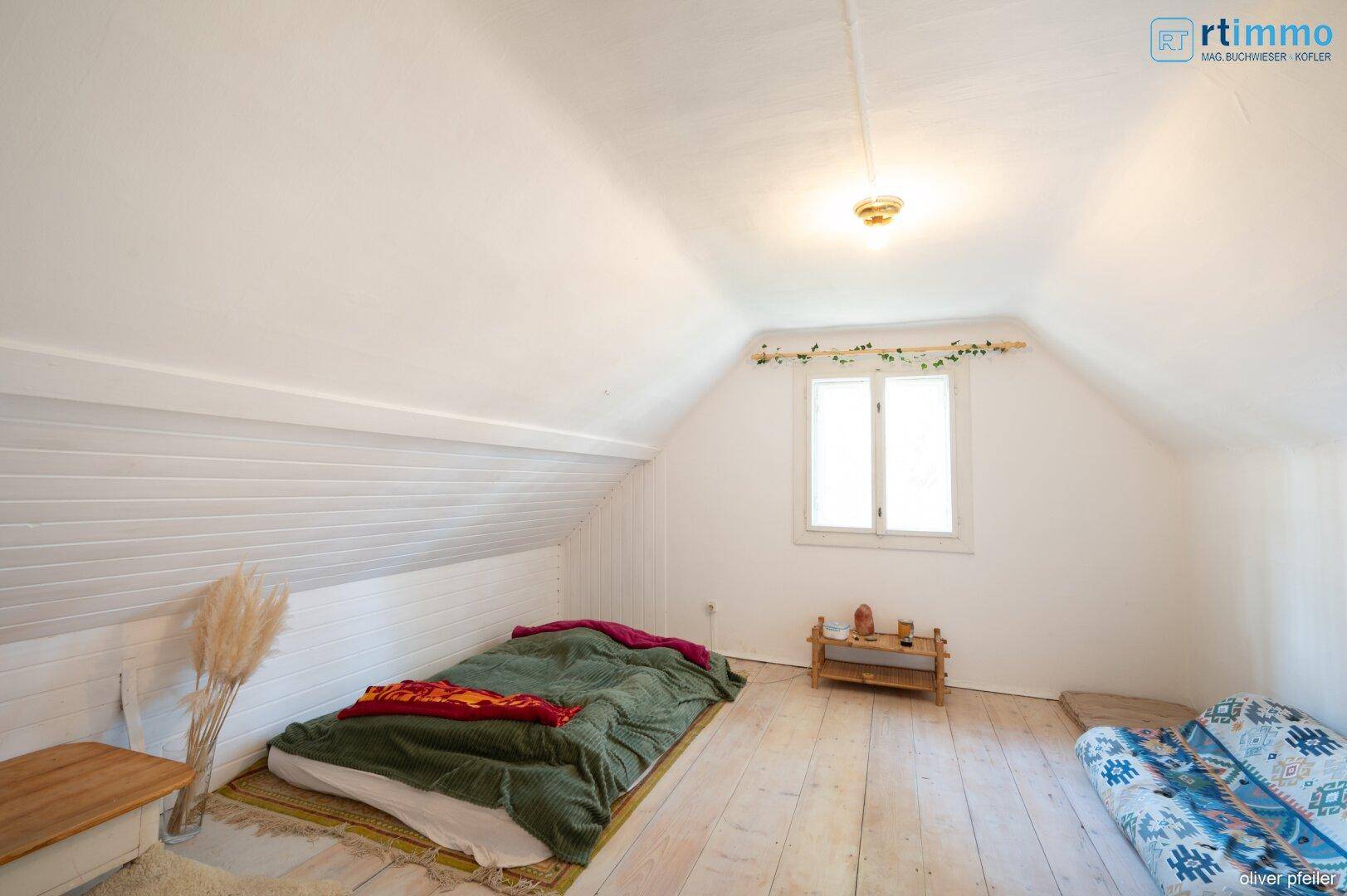 Helles Schlafzimmer im Dachgeschoss mit schrägen Wänden und Holzboden, einfach und gemütlich.