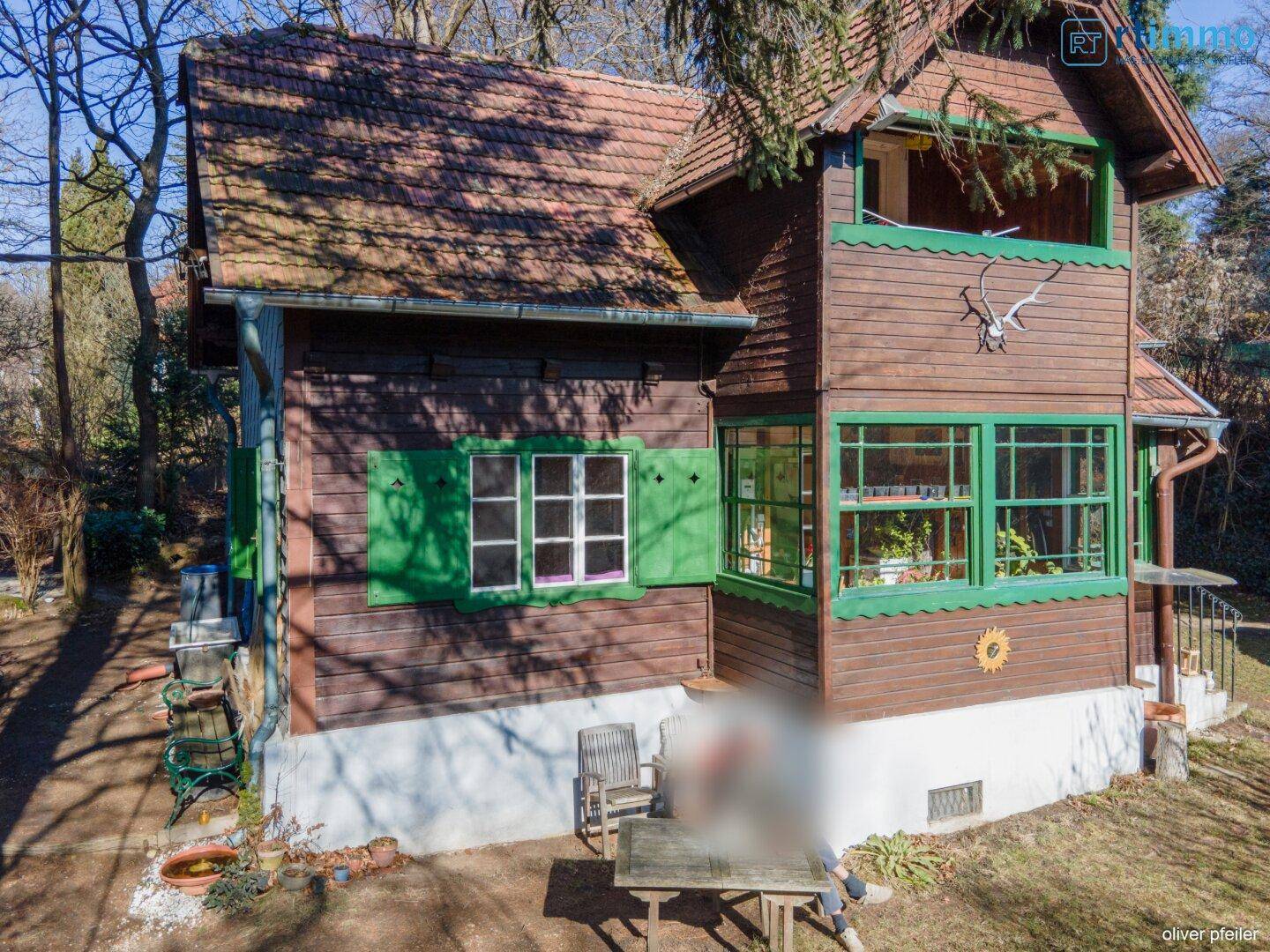 Charmantes Holzhaus mit grünen Fensterläden und einem sonnigen Sitzplatz im Gartenbereich.