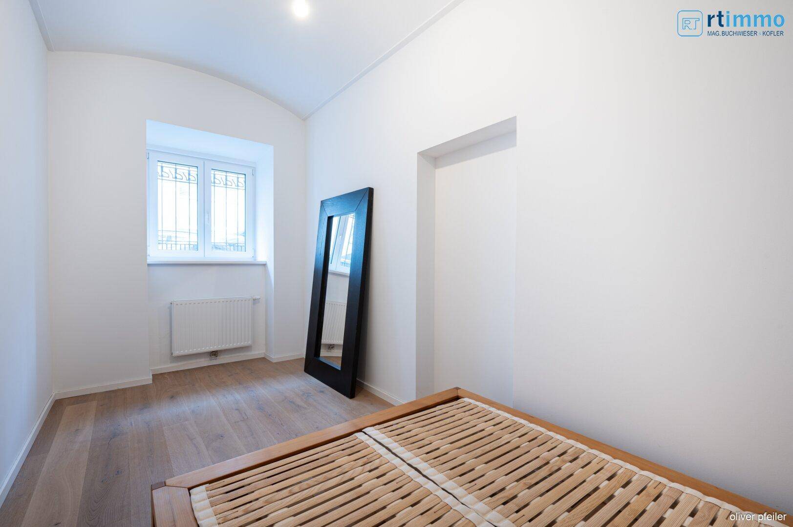Helles Schlafzimmer mit Holzboden, großem Spiegel und Fenster, bietet eine ruhige Atmosphäre.