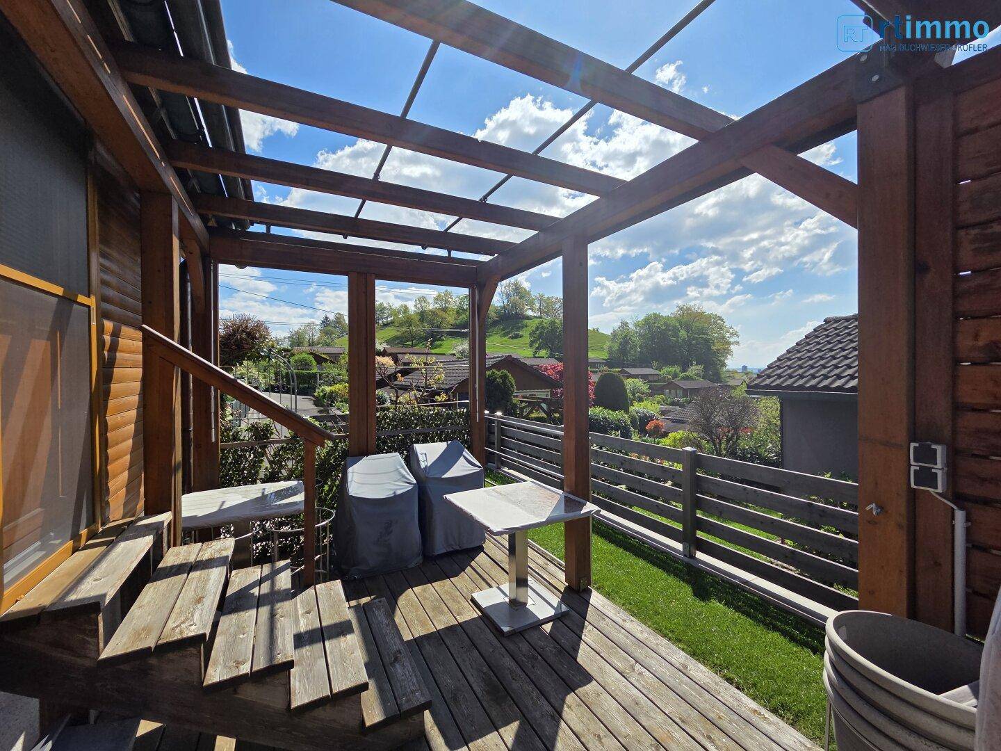 Überdachte Holzterrasse mit Sitzgelegenheiten und weitem Blick über die grüne Hügellandschaft.