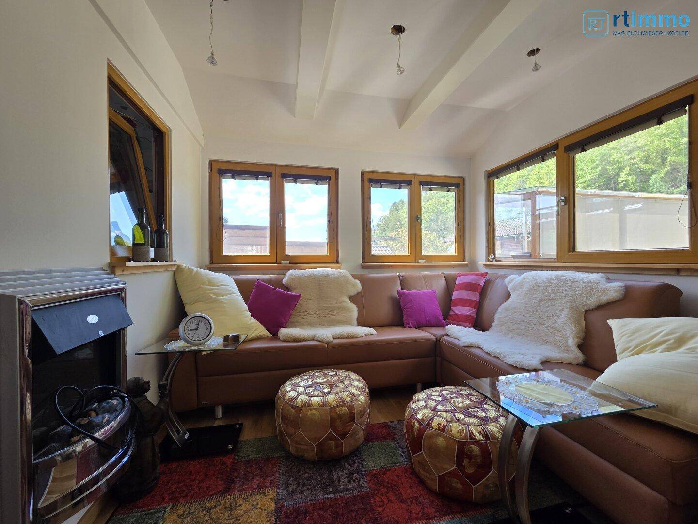 Gemütliches Wohnzimmer mit Ledersofa, bunten Teppichen und einem Kaminofen unter Holzbalkendecke.