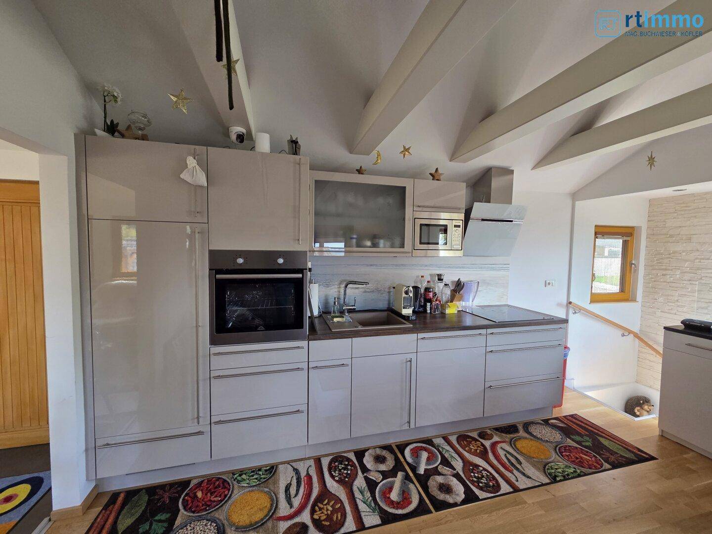 Moderne Einbauküche in hellem Design mit integrierten Geräten und Holzbalkendecke.
