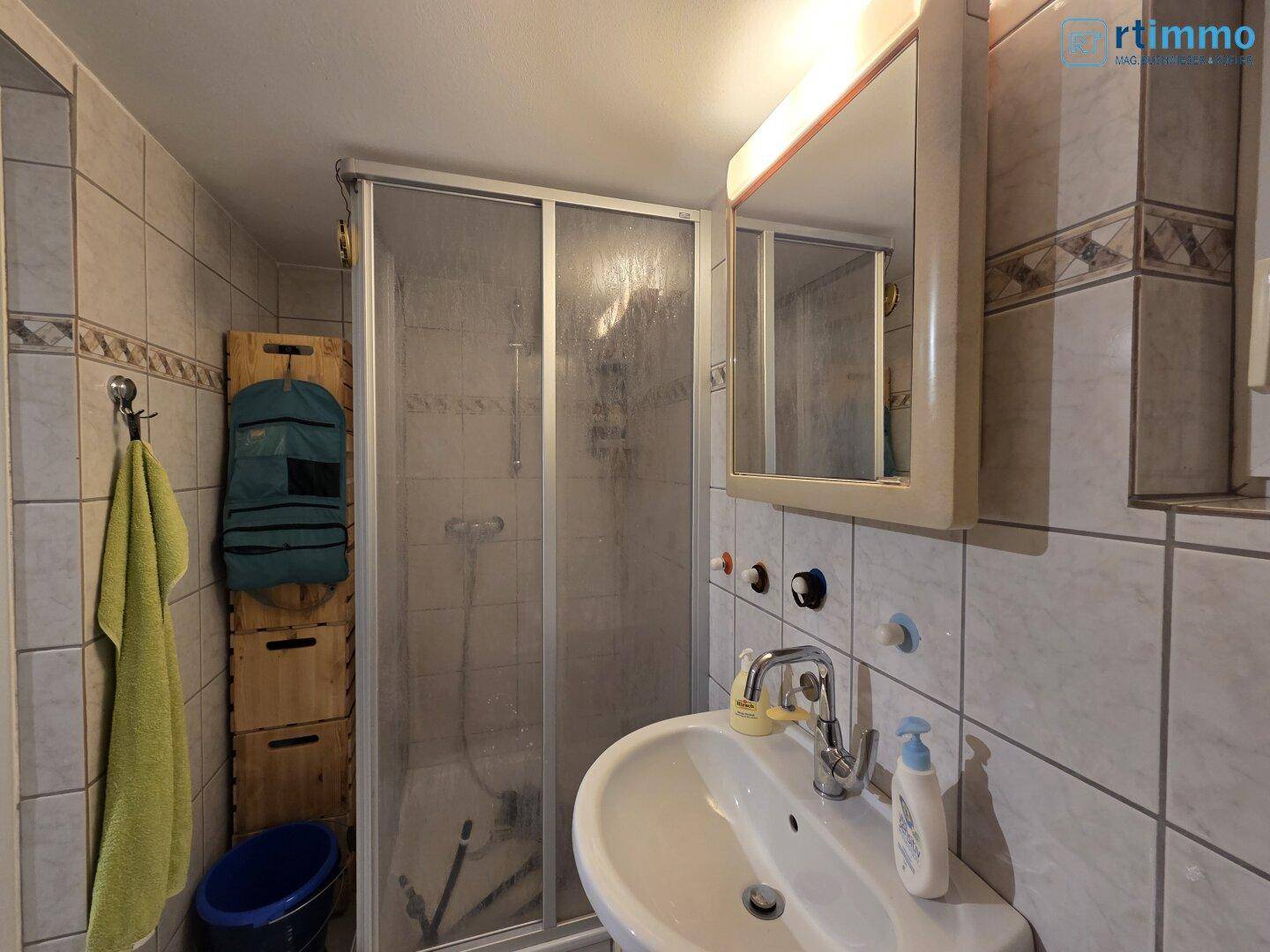 Gefliestes Badezimmer mit Duschkabine, Waschbecken und Spiegelschrank in hellem Design.