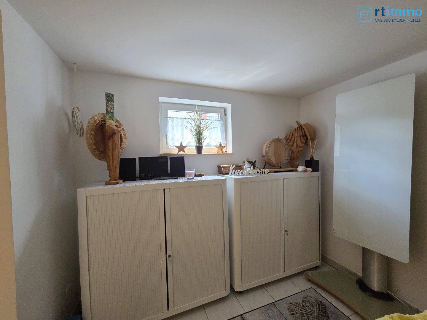 Helles Zimmer mit praktischen Schränken, einem Fenster und einem Infrarotheizpaneel an der Wand.