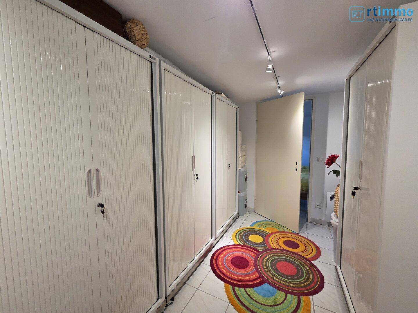 Langer Flur mit vielen Einbauschränken und einem bunten Teppich auf Fliesenboden.