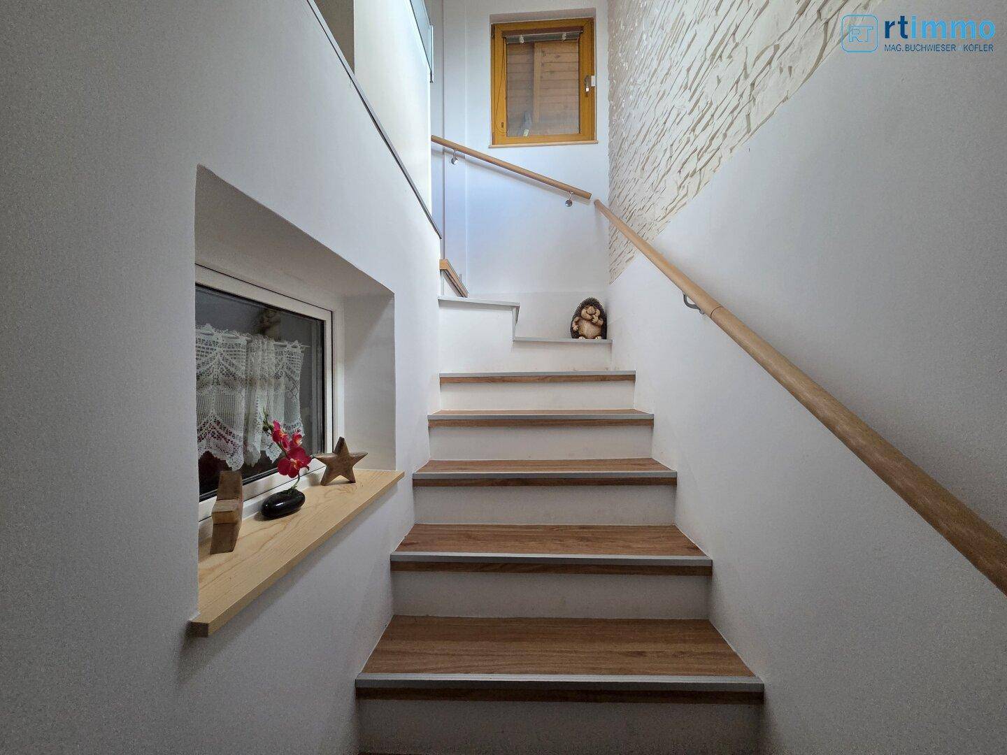 Helle Holztreppe mit Geländer und kleinen Fenstern, die natürliches Licht hereinlassen.