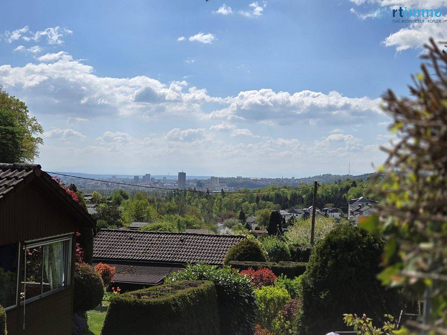 Weitläufiger Blick über die grüne Landschaft und die Dächer der umliegenden Häuser bis zur Stadt.
