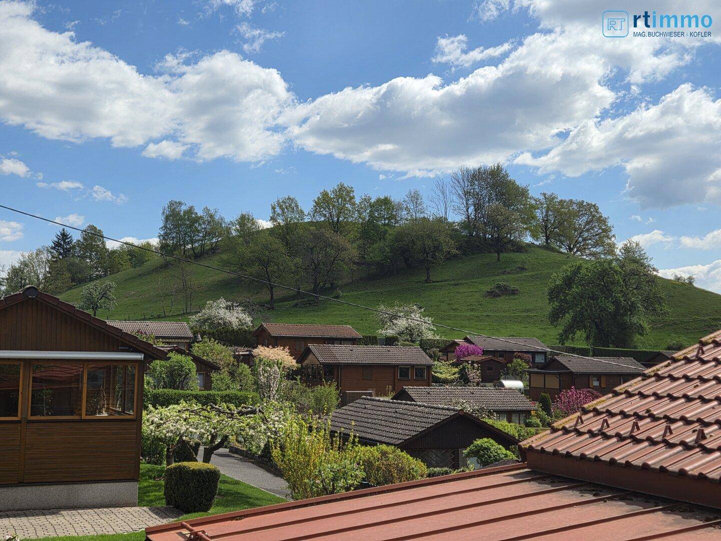 Panoramablick über die grüne Hügellandschaft und die Dächer der Häuser unter blauem Himmel.