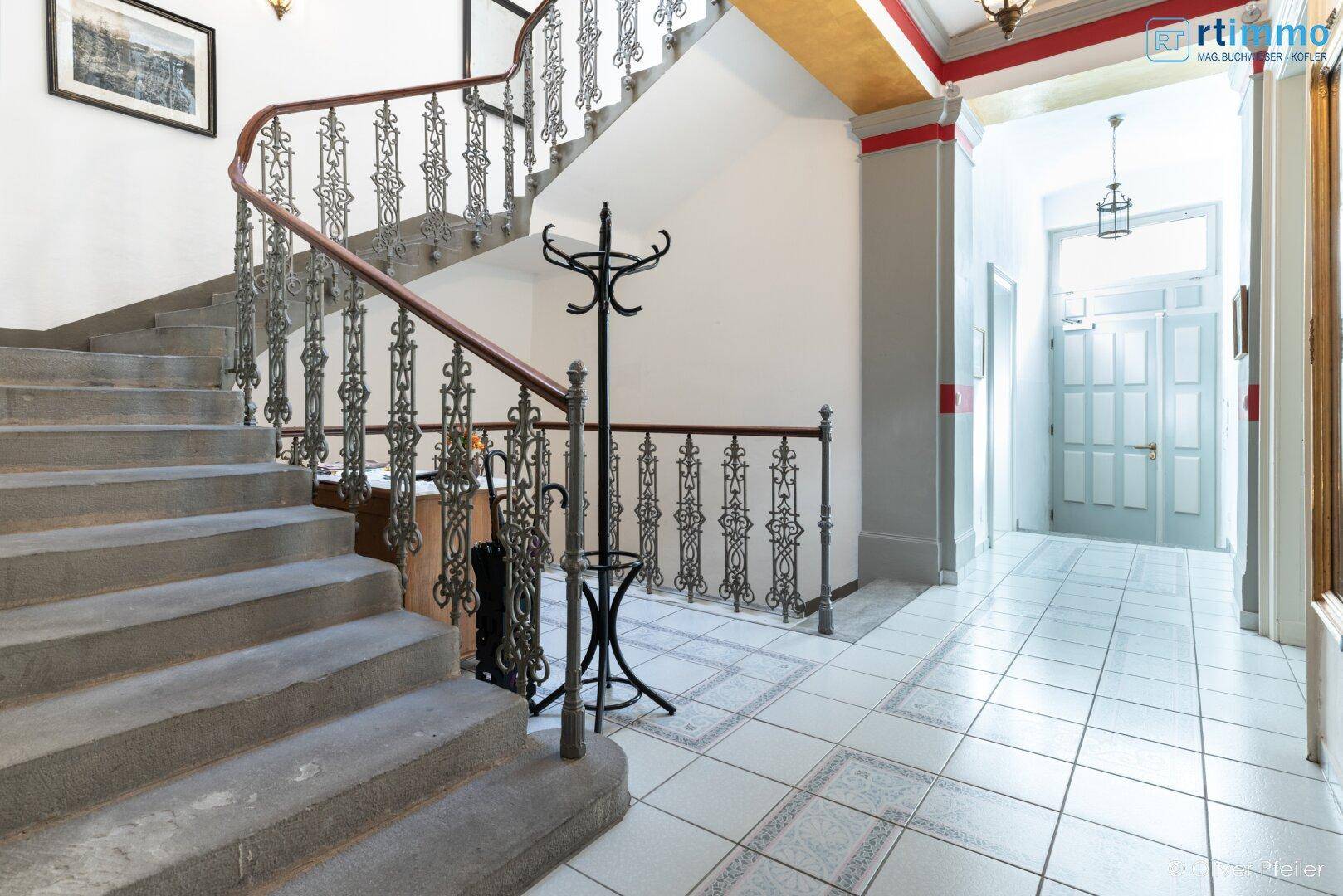 Geräumiger Flur mit historischer Treppe, Fliesenboden und Garderobe.