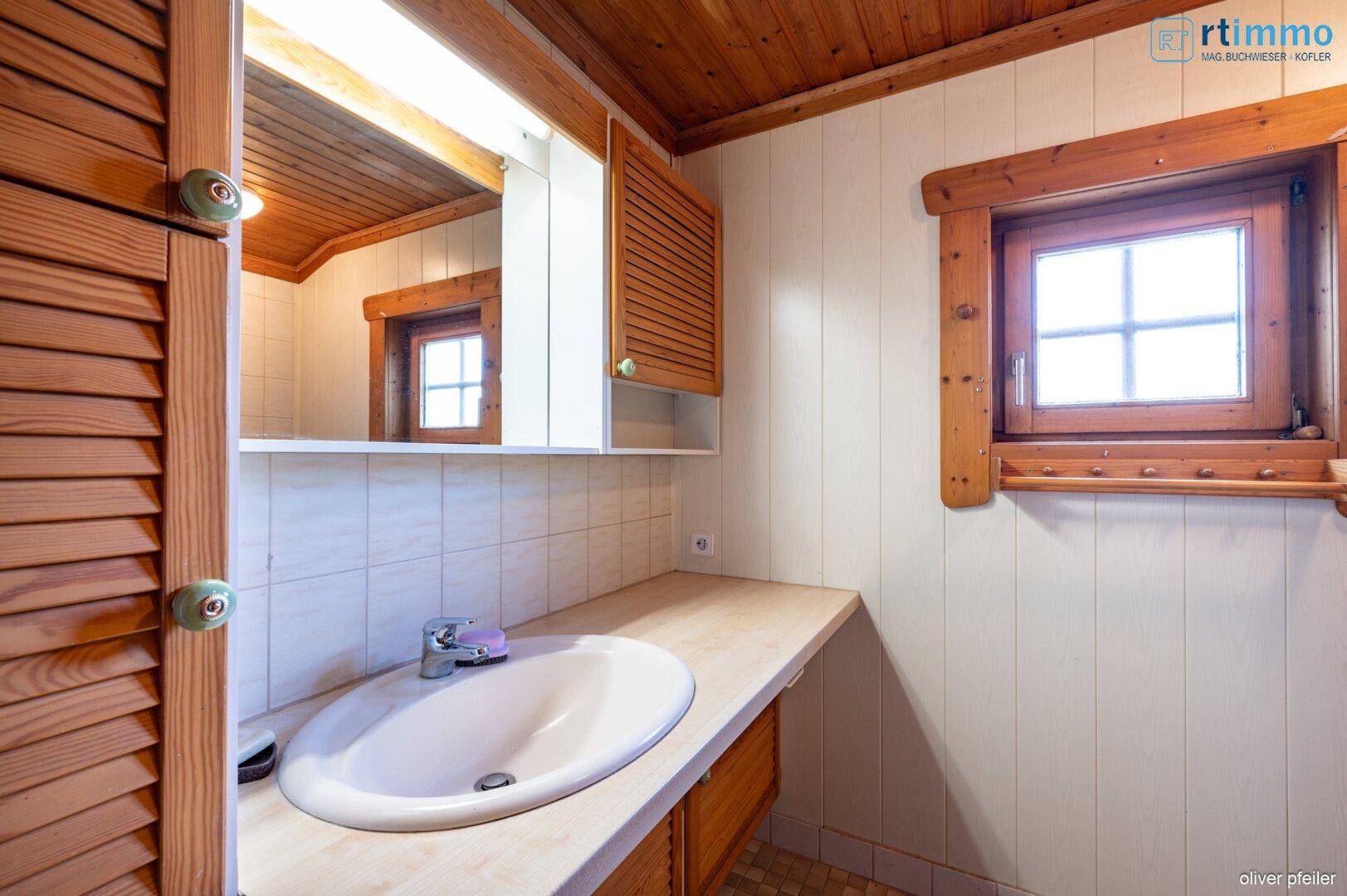 Badezimmer mit Einzelwaschbecken, Spiegelschrank und Holzverkleidung an Wänden und Decke.