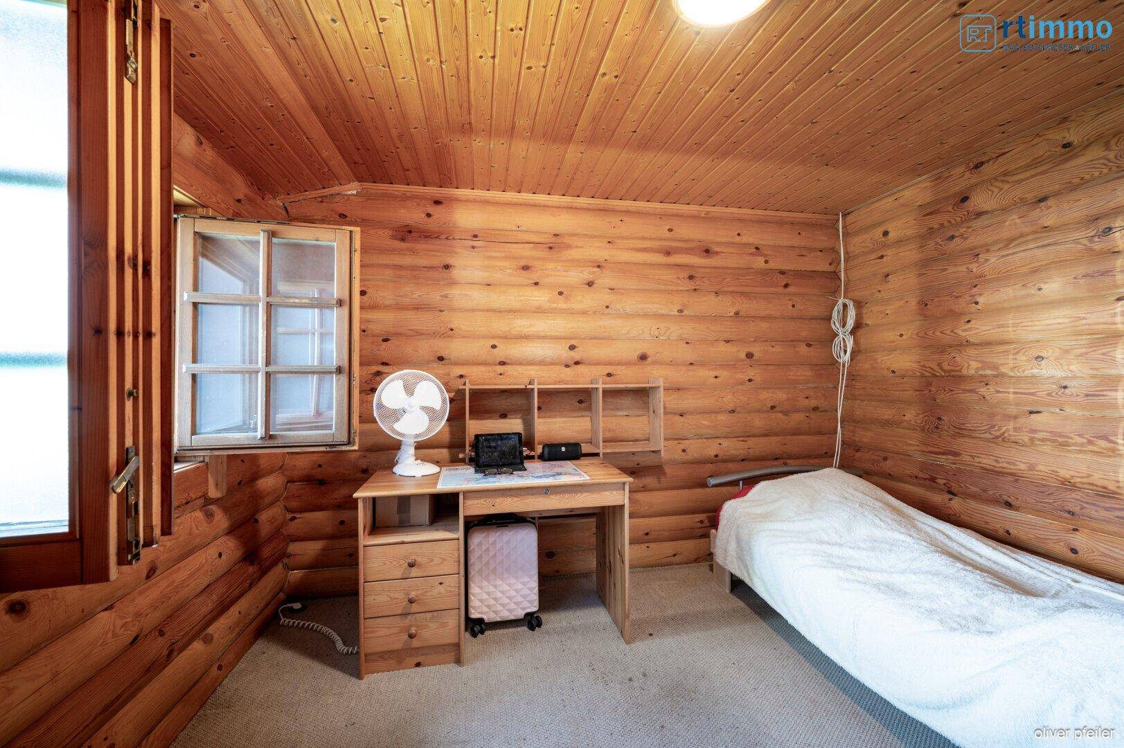 Gemütliches Schlafzimmer mit Holzwänden und -decke, ausgestattet mit einem Einzelbett und einem Schreibtisch.