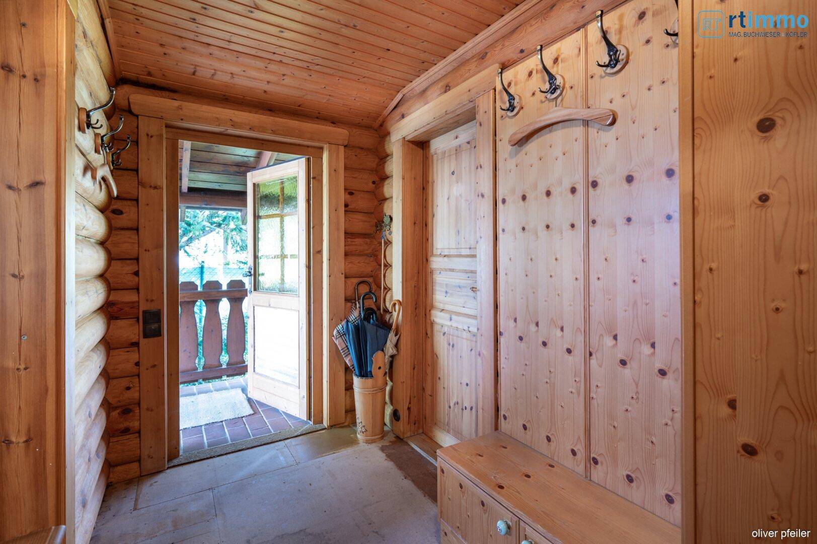 Rustikaler Eingangsbereich mit Holzwänden und -boden, Garderobe und Zugang zu einem überdachten Außenbereich.