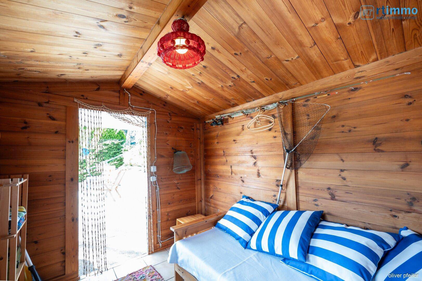 Kleiner Raum mit Holzwänden und -decke, ausgestattet mit einem Tagesbett und direktem Zugang ins Freie.