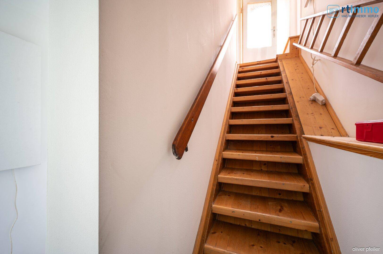 Holztreppe führt in das obere Stockwerk, mit natürlichem Lichteinfall durch die Tür.