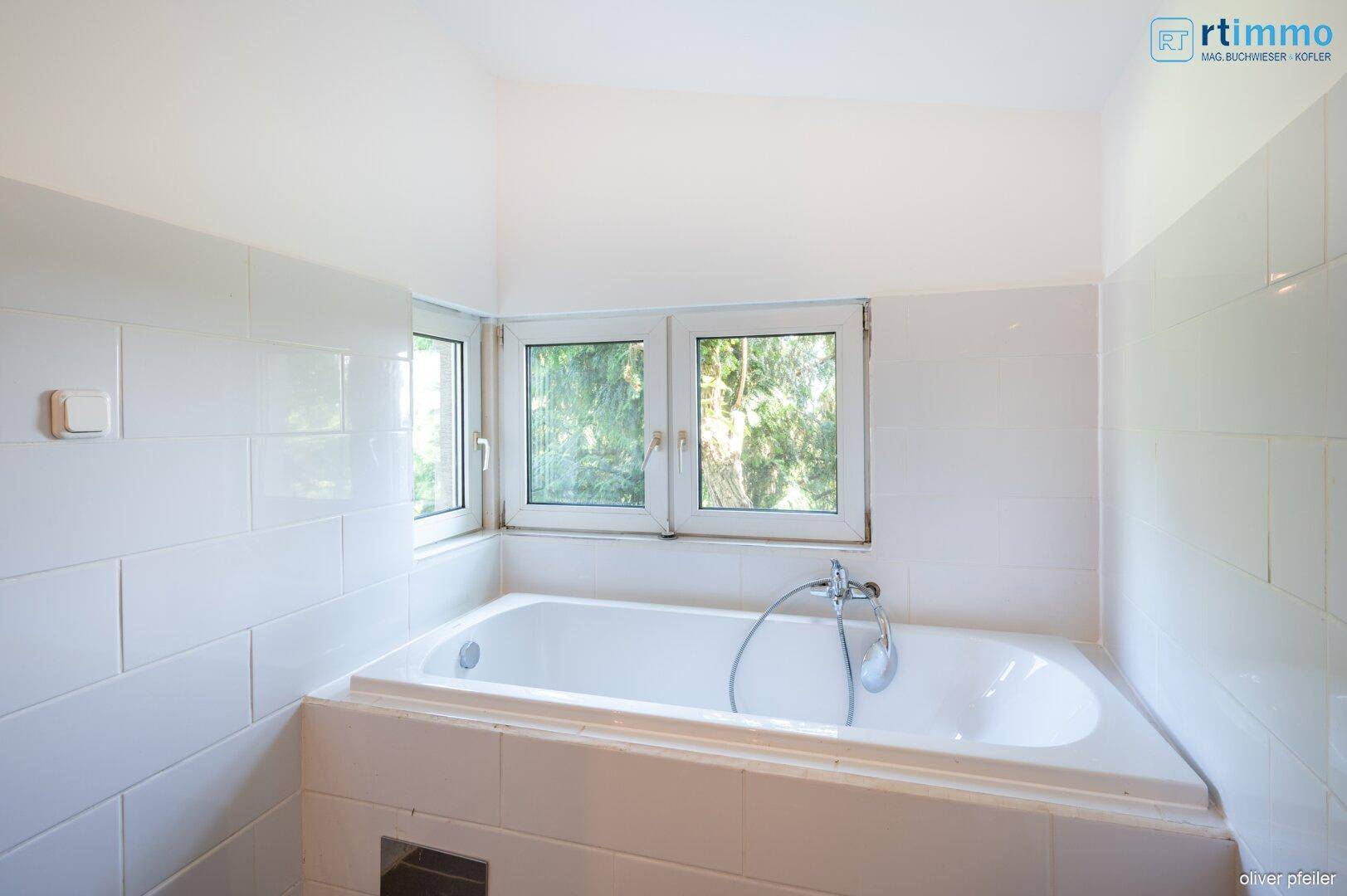 Badezimmer mit eingebauter Badewanne und Fenster, hell gefliest.