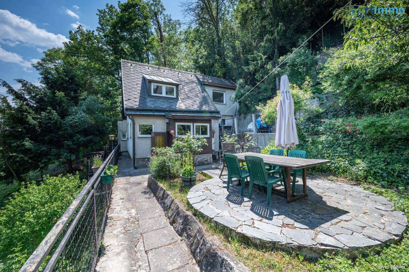 Hausansicht mit Steinterrasse und Essbereich im sonnigen Garten.
