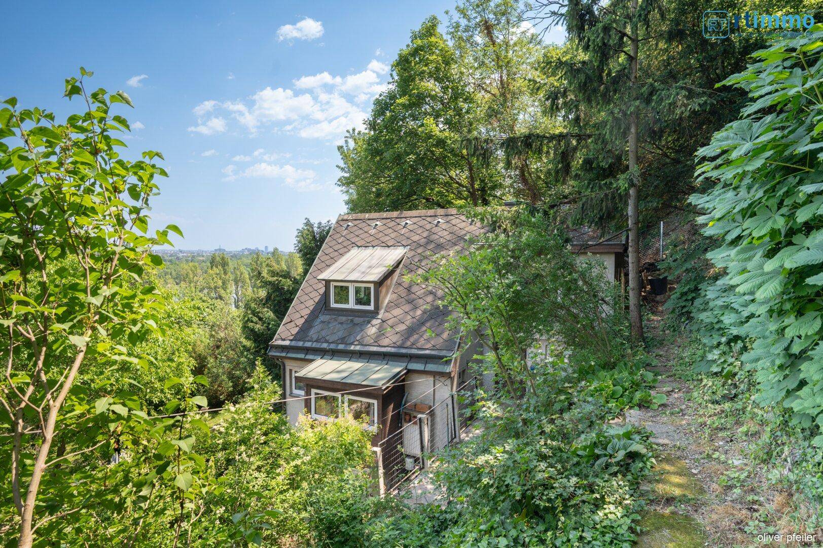 Haus eingebettet in eine grüne Hügellandschaft mit vielen Bäumen.