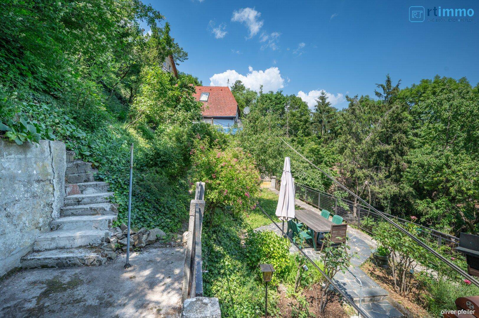 Terrassenbereich mit Steintreppe und Blick auf den grünen Garten und weitere Häuser.