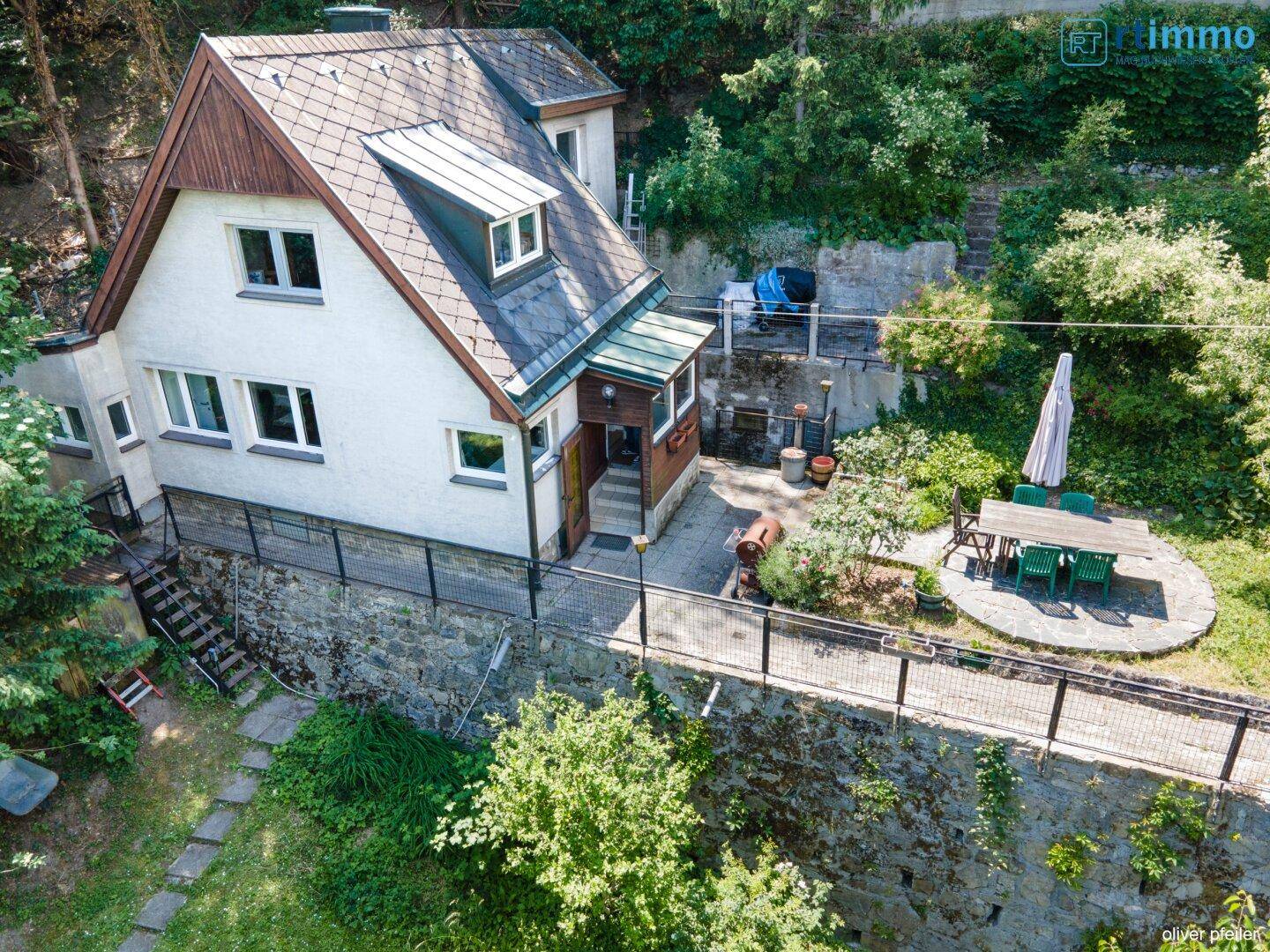 Ansicht des Hauses mit einer Steinterrasse und einem Essbereich im grünen Garten.