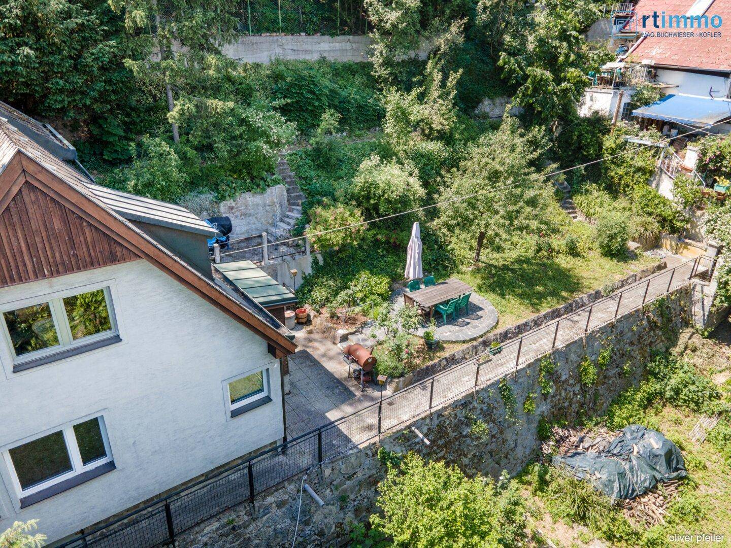 Seitlicher Blick auf das Haus mit einer gepflasterten Terrasse und einem Essbereich im Garten.