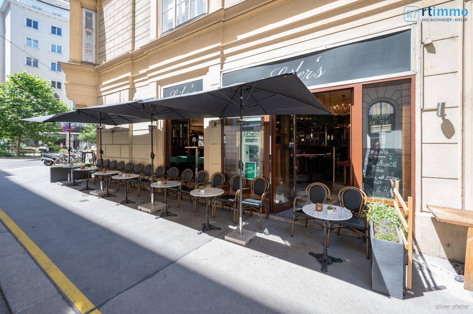 Weitläufige Außenterrasse eines Cafés mit vielen Tischen und großen schwarzen Sonnenschirmen.