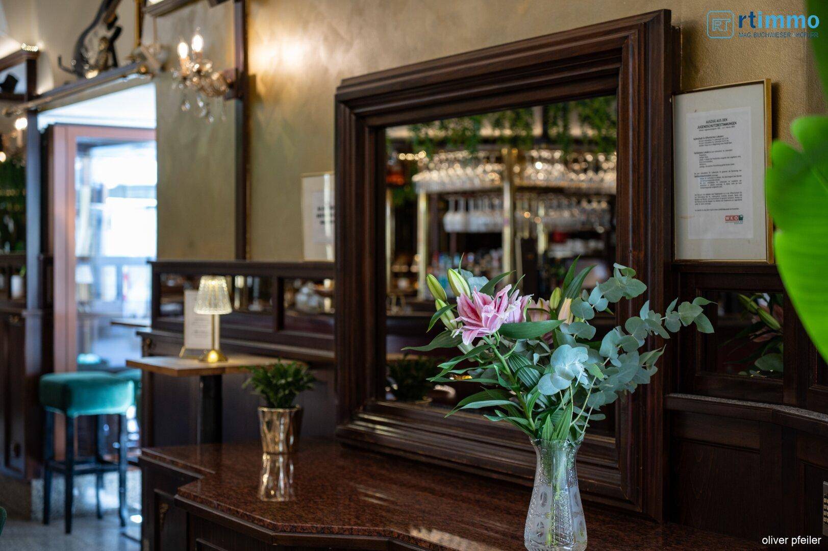 Ein großer Holzspiegel mit Blumenarrangement und einer kleinen Lampe im Barbereich.