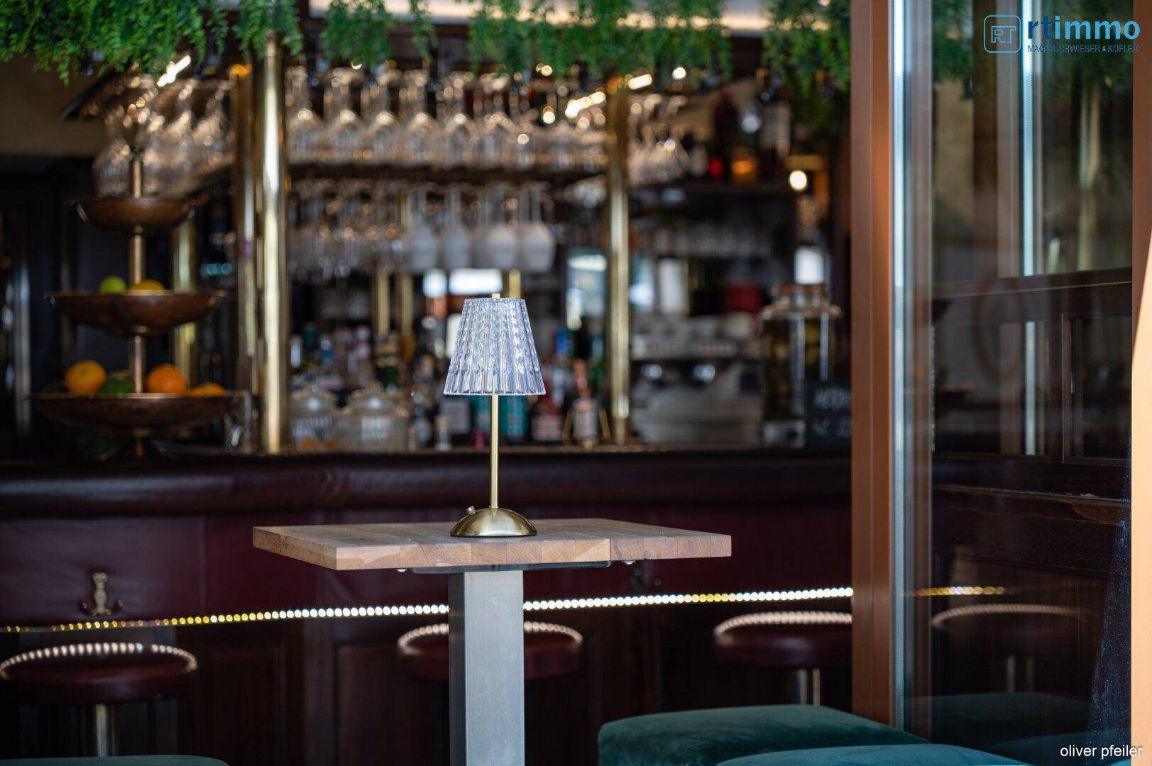 Nahaufnahme eines kleinen Tisches mit Lampe und Blick auf den Barbereich im Hintergrund.