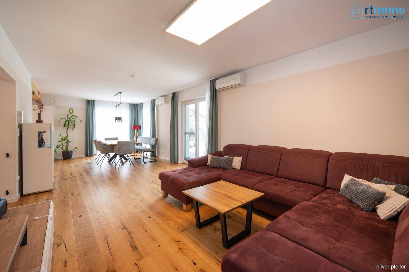 Geräumiger Wohnbereich mit großem Ecksofa und Essbereich im Hintergrund, mit Holzboden.