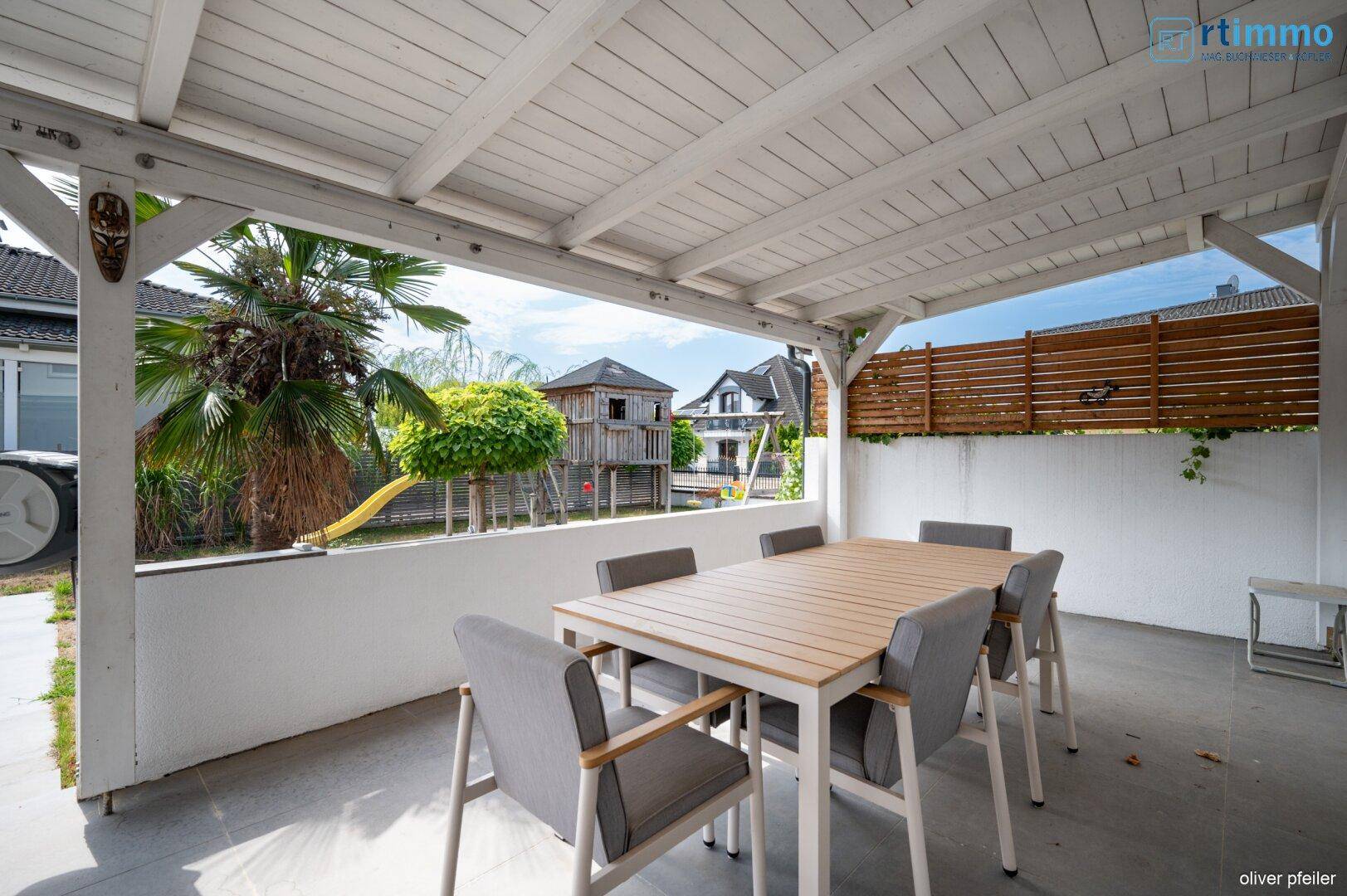Gemütliche überdachte Terrasse mit Essbereich und Blick auf den Spielplatz im Garten.