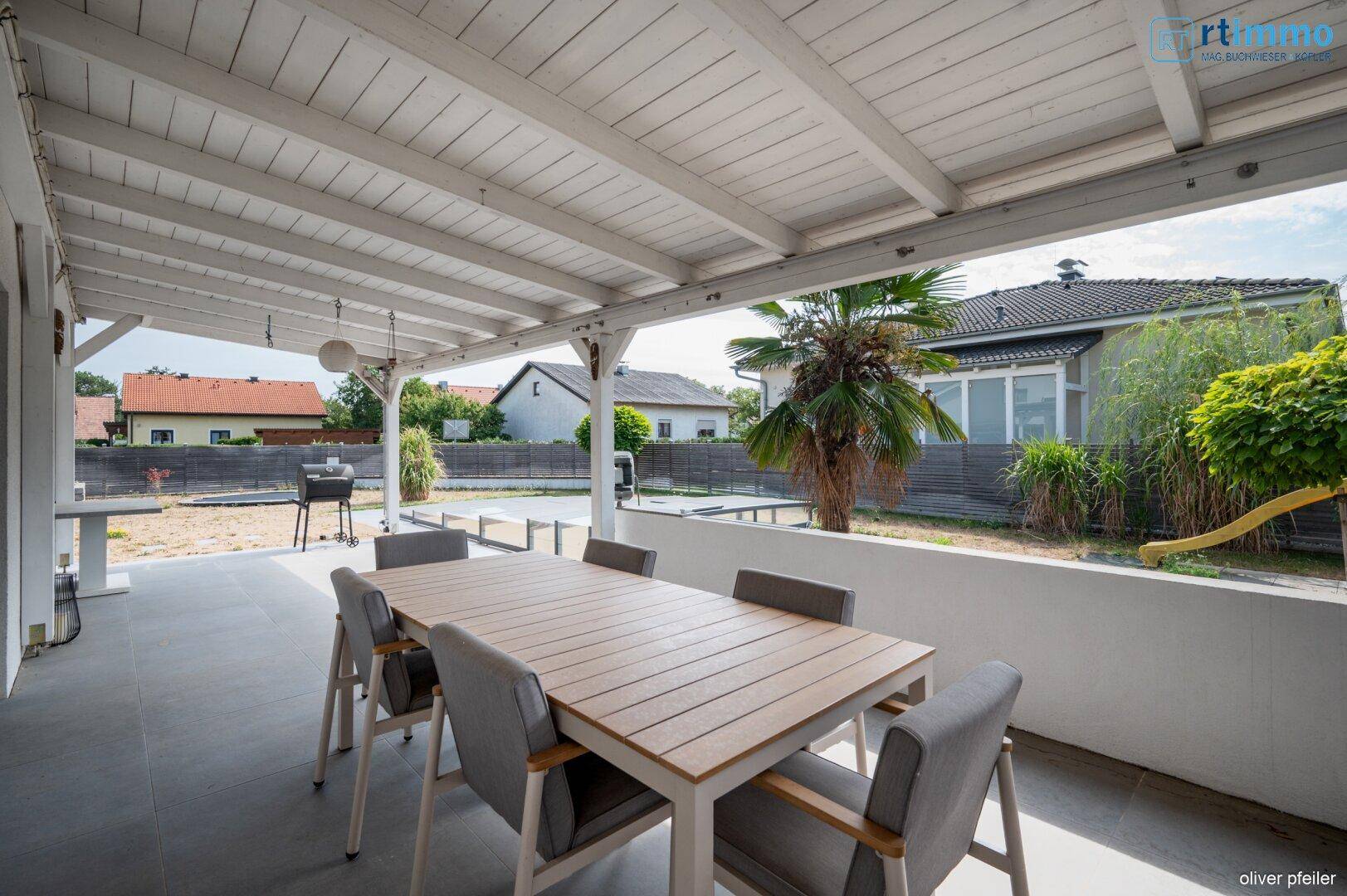 Überdachte Terrasse mit Esstisch und Stühlen, ideal für Mahlzeiten im Freien.