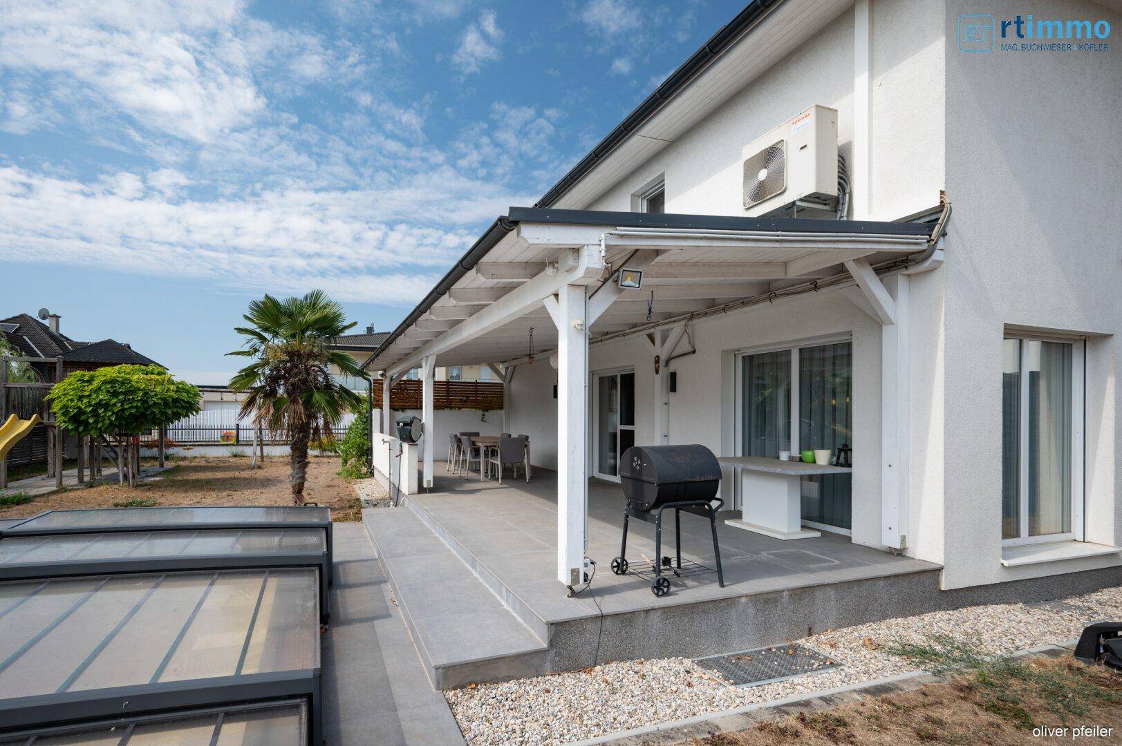 Hausansicht mit überdachter Terrasse, Grillbereich und Zugang zum Garten.