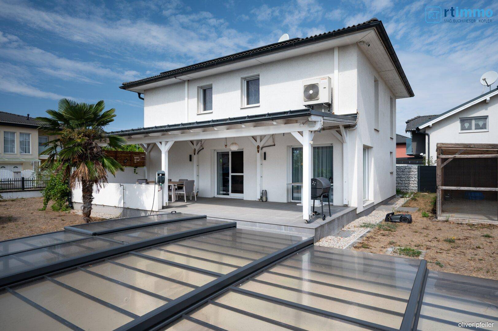 Seitenansicht des Hauses mit überdachter Terrasse und dem geschlossenen Poolbereich.