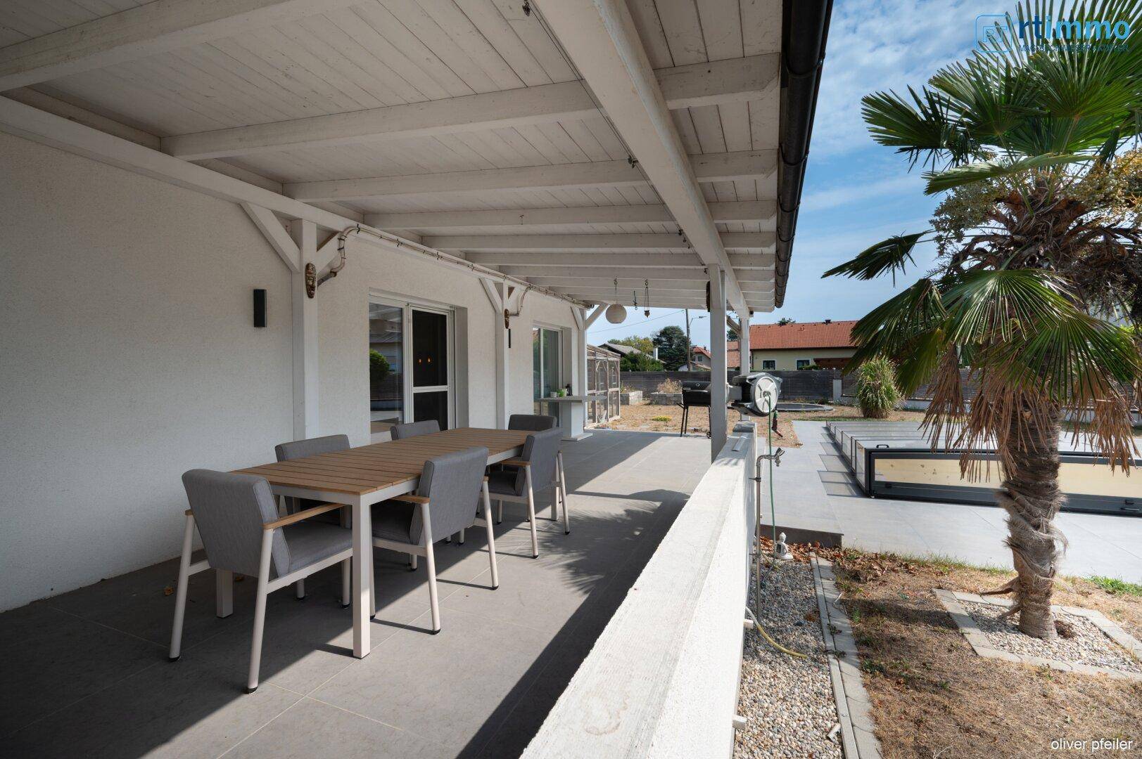 Überdachte Terrasse mit Essbereich und Blick auf den Pool und den Garten.