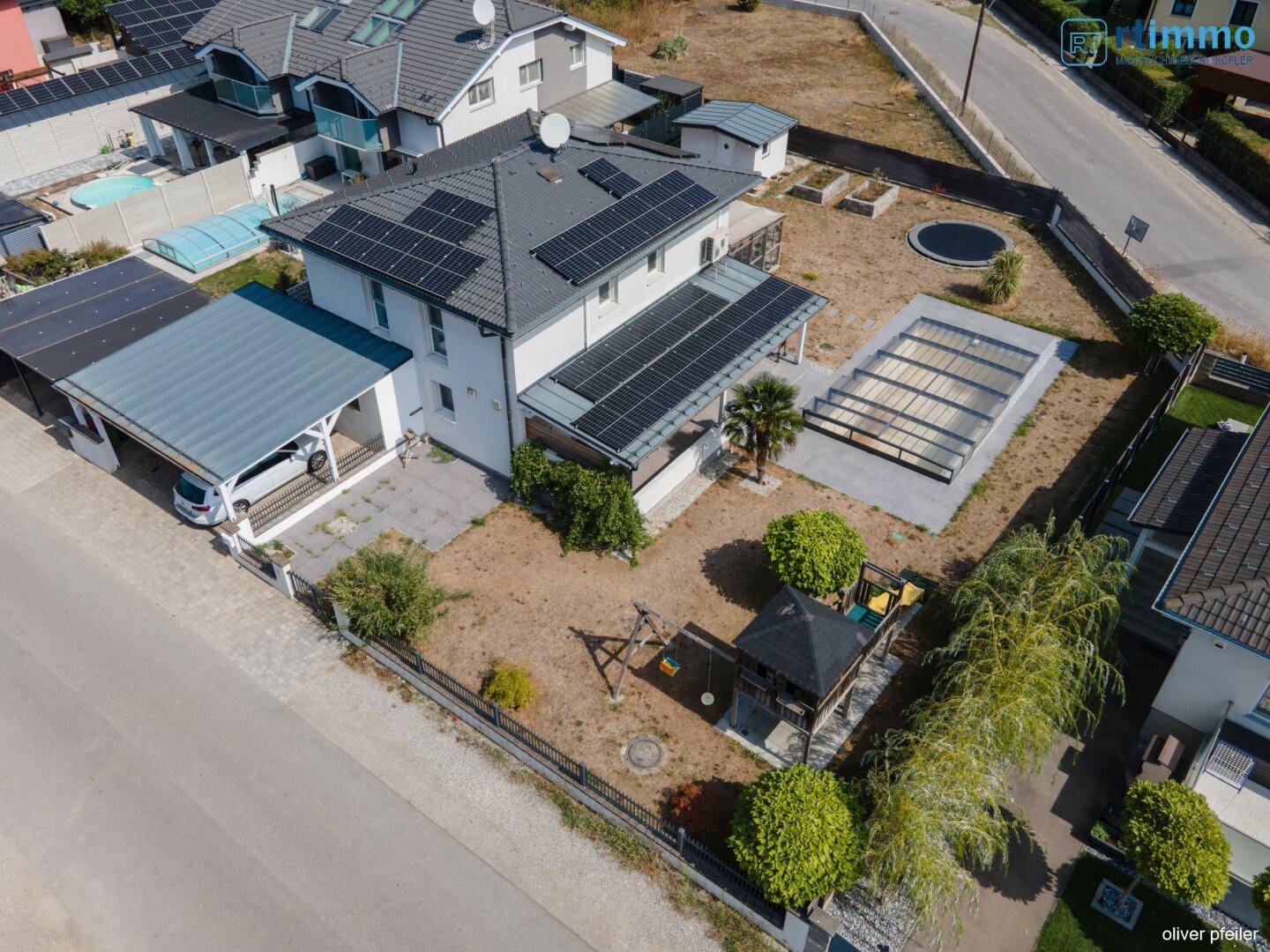 Luftaufnahme eines Einfamilienhauses mit Solaranlage, Garten und Poolbereich in einer Wohnsiedlung.