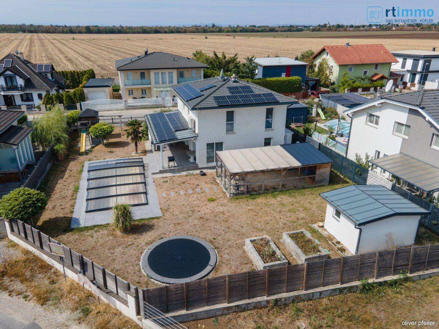 Weitläufiger Gartenbereich eines Hauses mit Trampolin, Hochbeeten und überdachtem Pool.