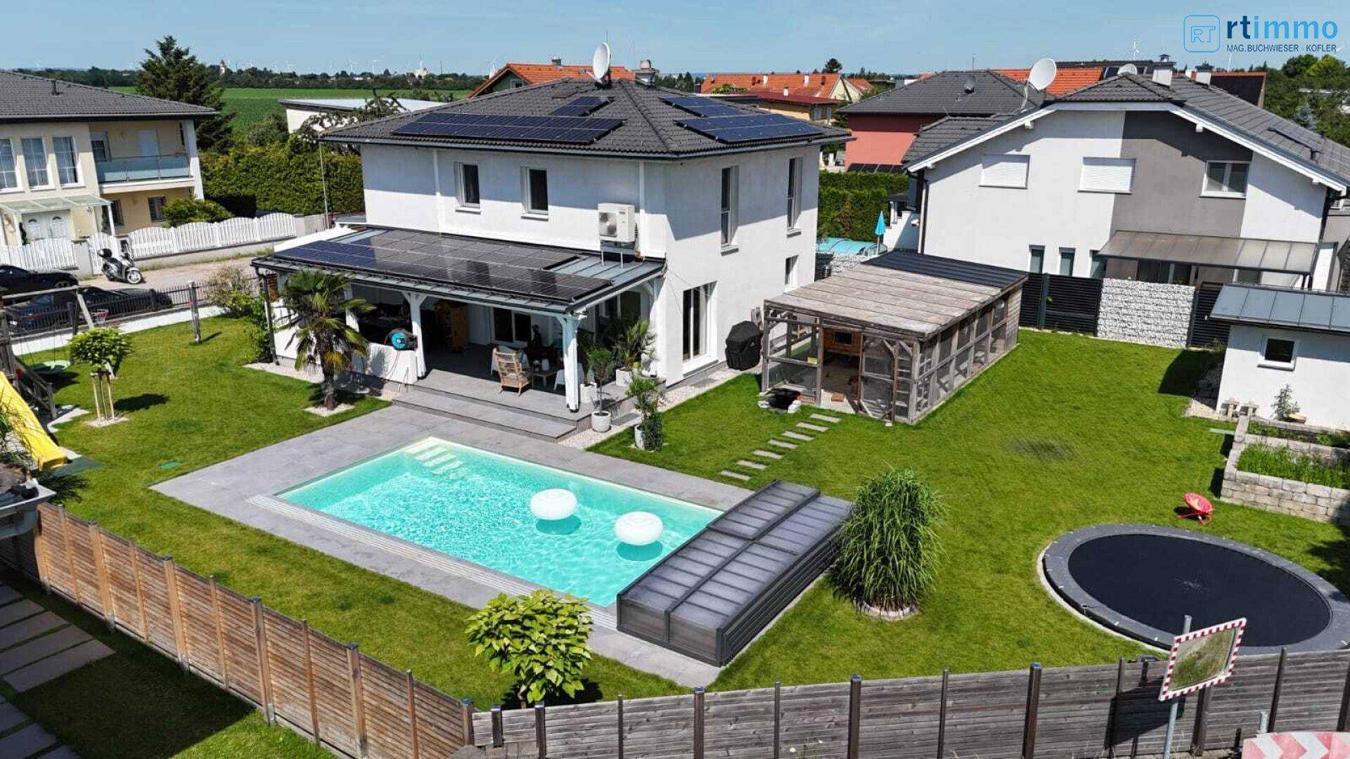 Gepflegter Garten mit großem Pool, Rasenfläche und Spielgeräten hinter dem modernen Haus.