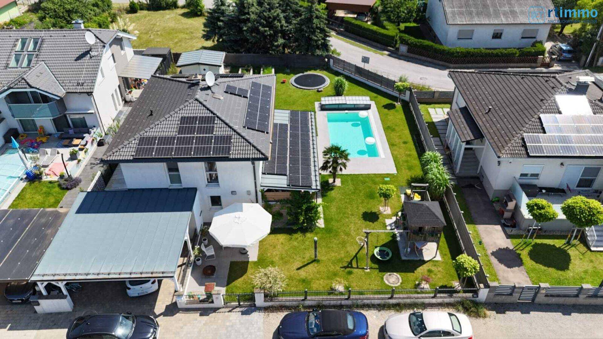 Vogelperspektive eines Wohnhauses mit Garten, Pool, Solaranlage und Carport in einer Wohnsiedlung.