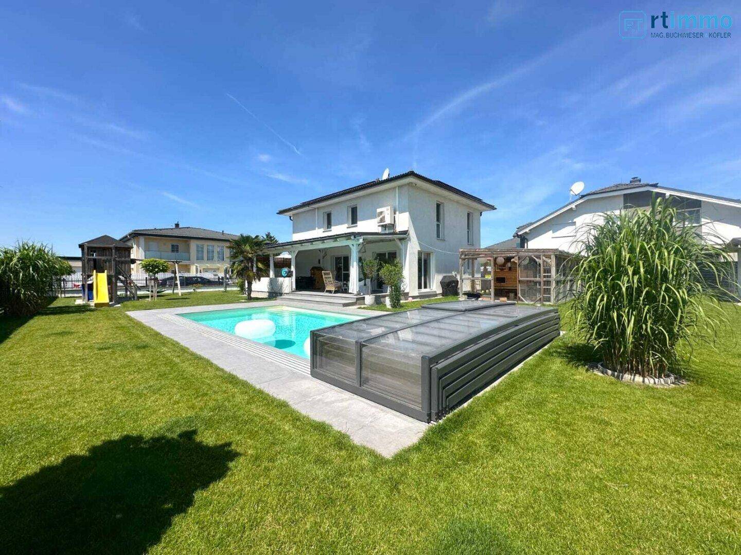 Ansicht des Hauses von der Gartenseite mit großem Pool und gepflegter Rasenfläche unter blauem Himmel.