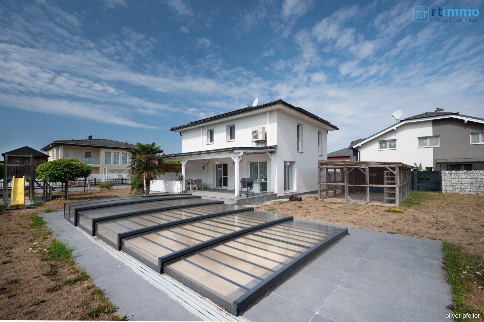 Hausansicht von der Gartenseite mit überdachtem Poolbereich und großer Terrasse.
