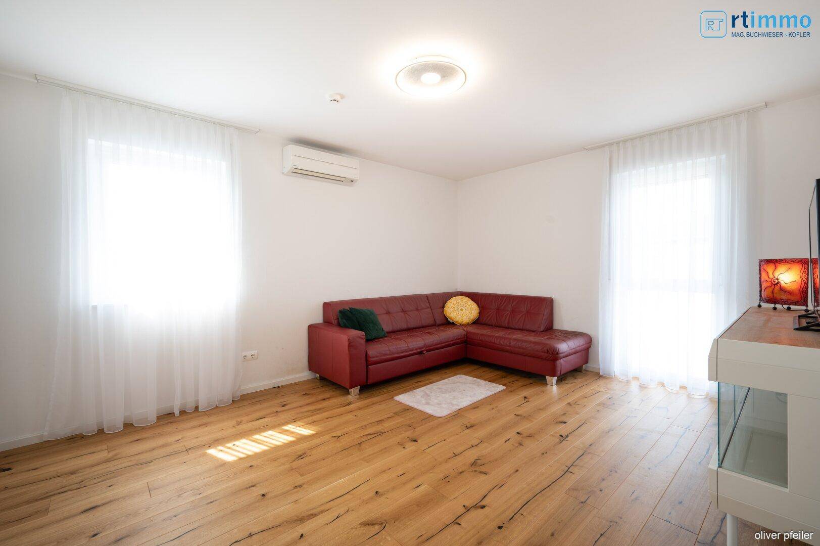 Helles Wohnzimmer mit rotem Ecksofa und Holzboden, durch große Fenster lichtdurchflutet.