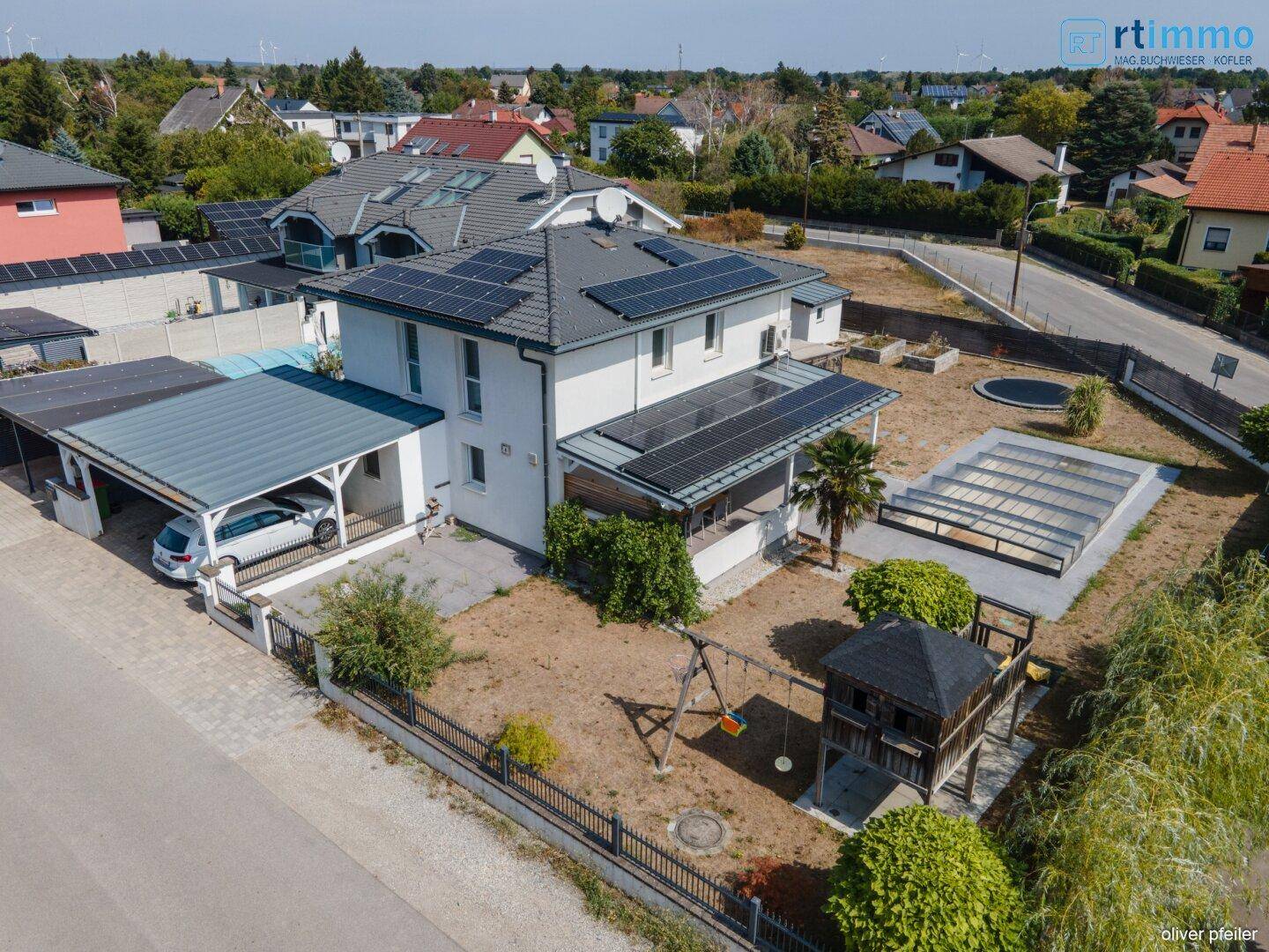 Luftaufnahme des Hauses mit Garten, Carport, Poolbereich und Spielplatz.