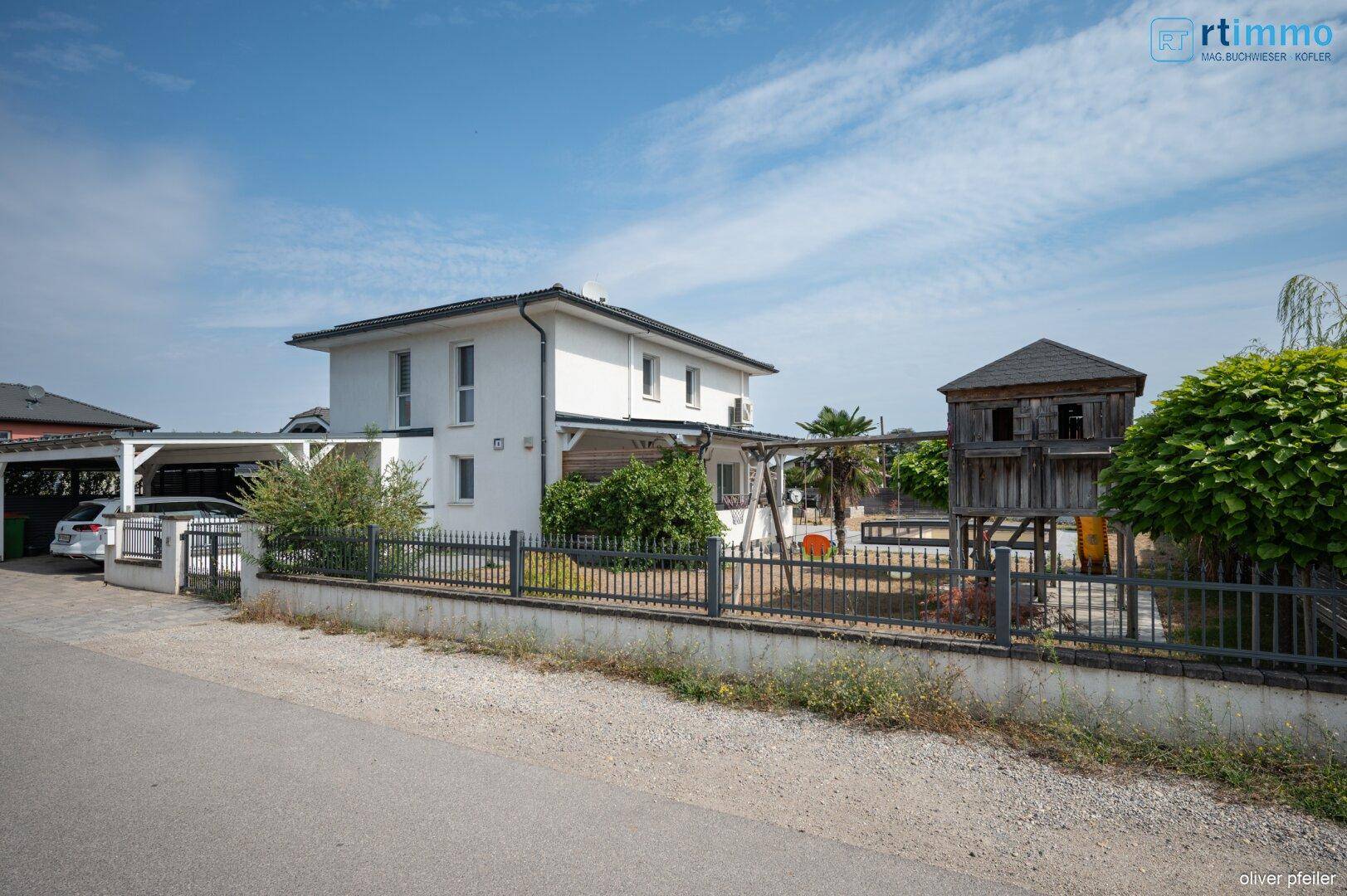 Ansicht des Hauses von der Straße mit Vorgarten, Zaun und Carport.