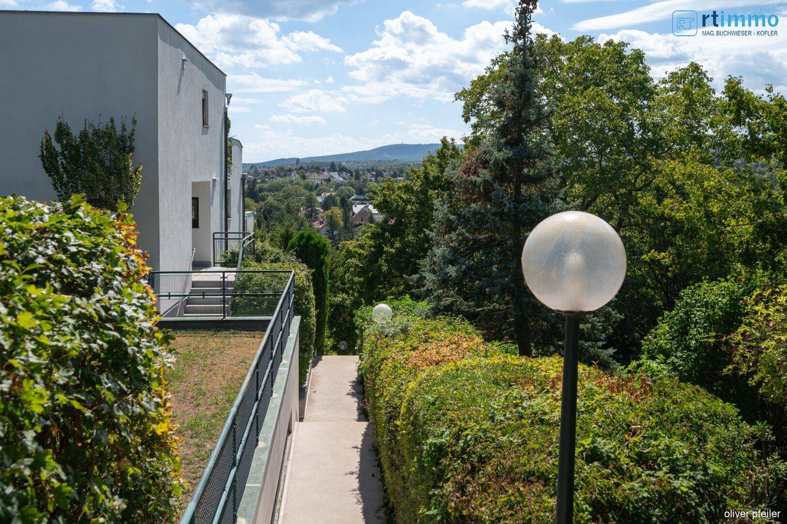 Außenbereich mit Treppe, viel Grün und einem Weg, der zu weiteren Gebäudeteilen führt.