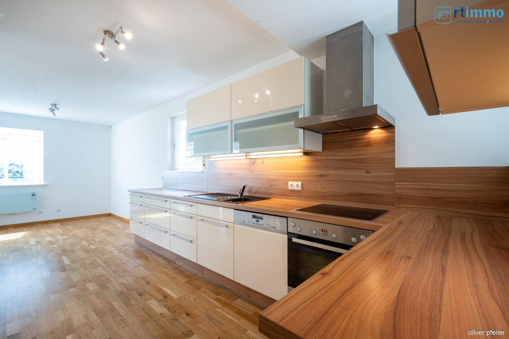 Moderne Küche mit beigen Hochglanzfronten, Holzarbeitsplatte und integrierten Geräten.