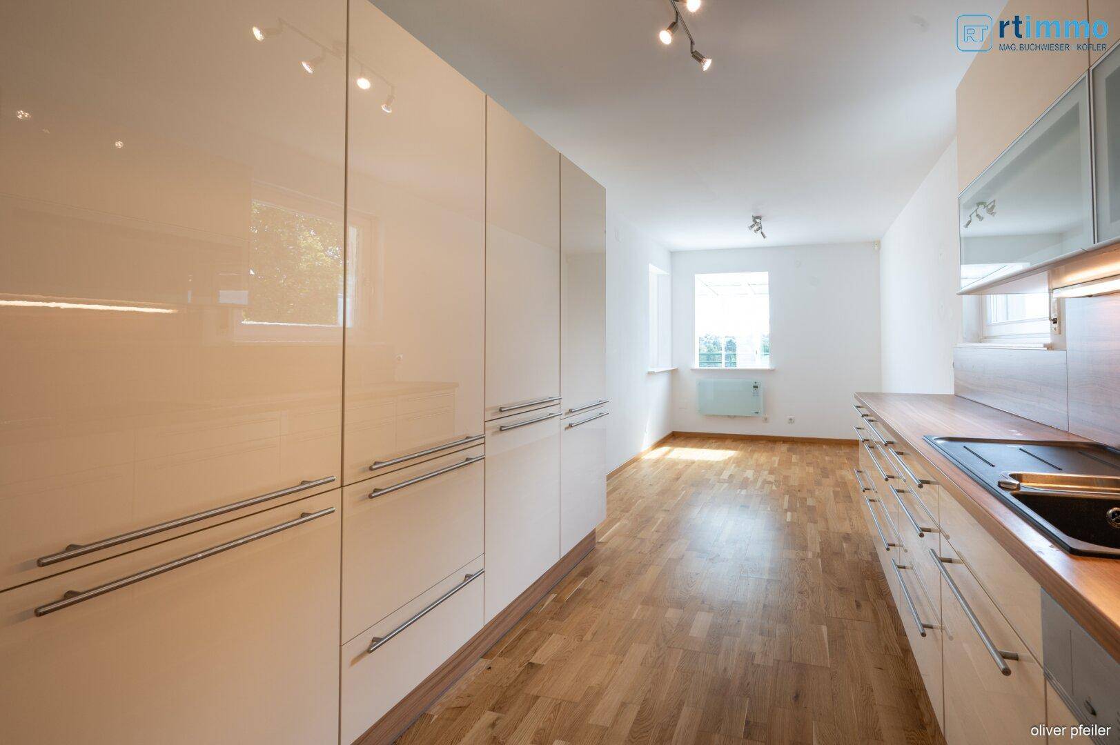 Geräumige Küche mit viel Stauraum in beigen Hochglanzschränken und Holzboden.