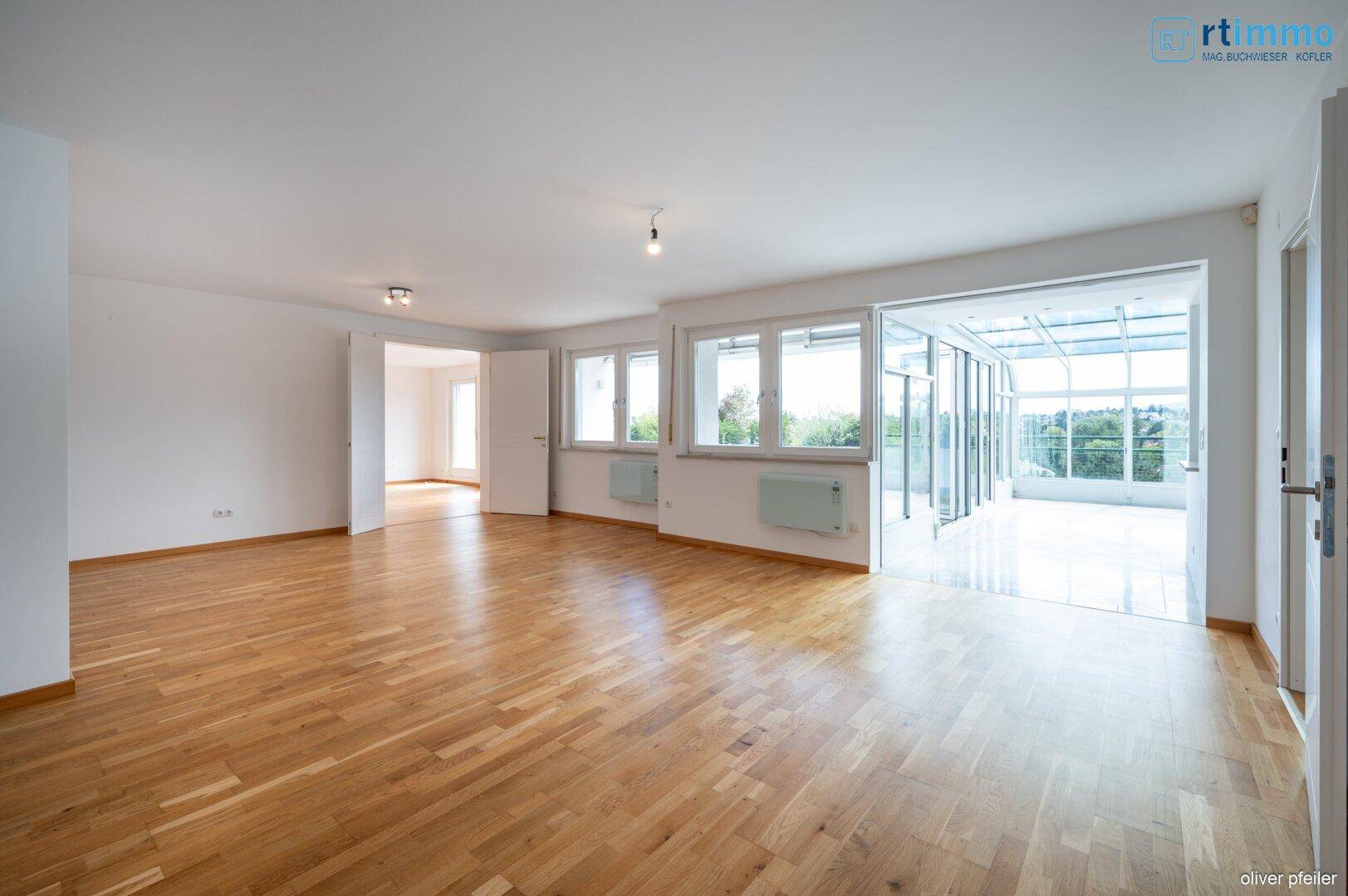 Helles Wohnzimmer mit Parkettboden und Zugang zu einem lichtdurchfluteten Wintergarten.