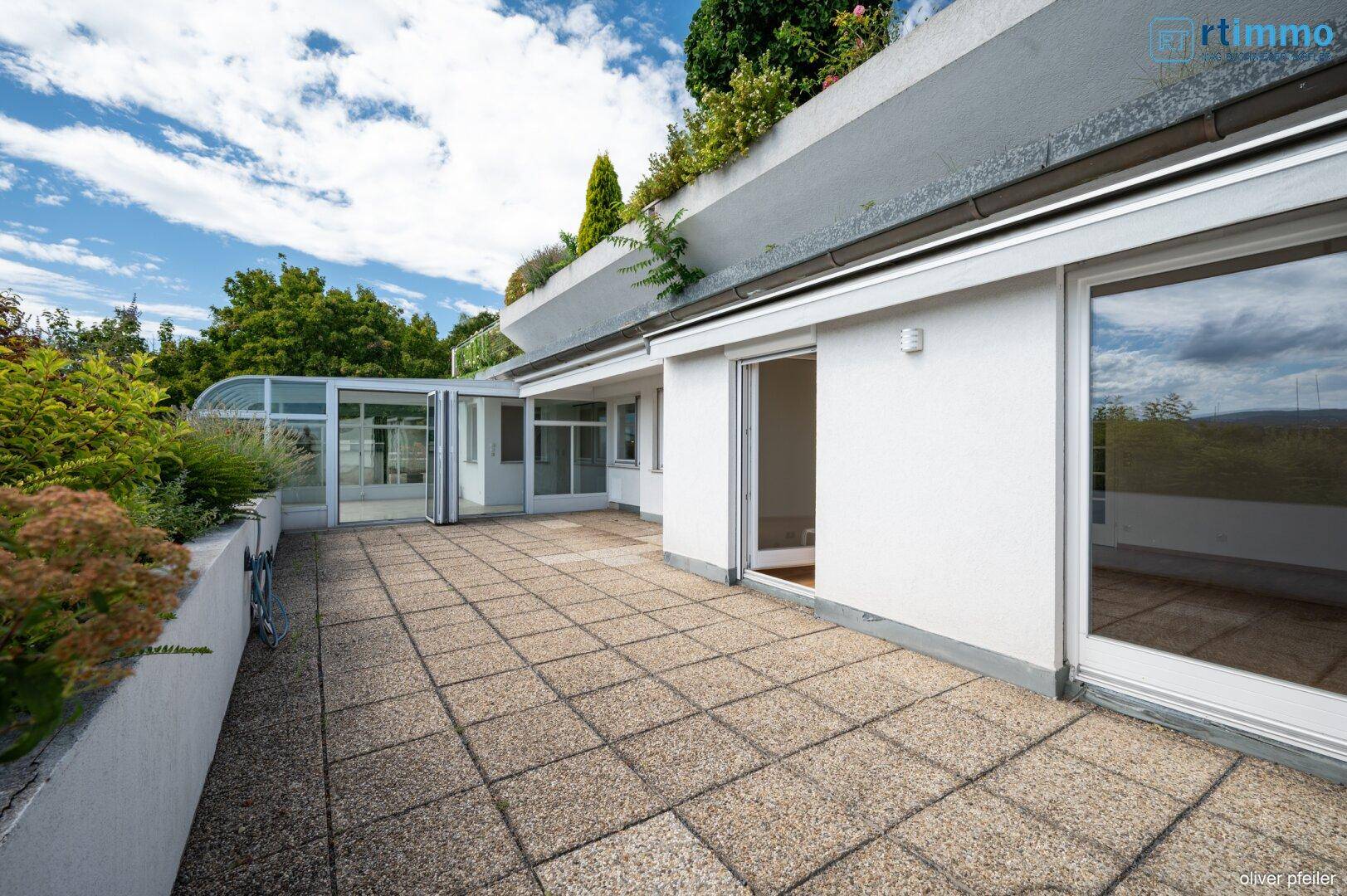 Große gepflasterte Terrasse mit viel Grün und Zugang zum Wintergarten.